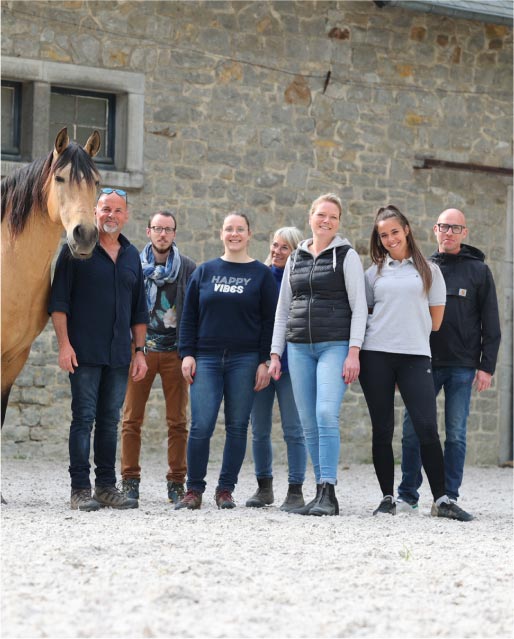 Un groupe de personnes debout à côté d'un cheval devant une écurie après une session de travail sous la thématique "Cohésion de groupe"