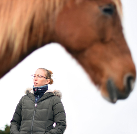 Une femme en gros plan qui observe quelque chose ou quelqu'un avec un cheval flou en arrière-plan