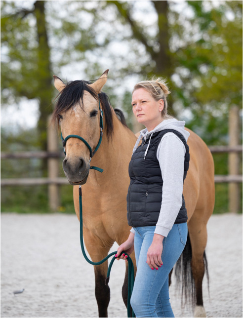 Une femme debout à côté d'un cheval de couleur brun clair avec une crinière noire.